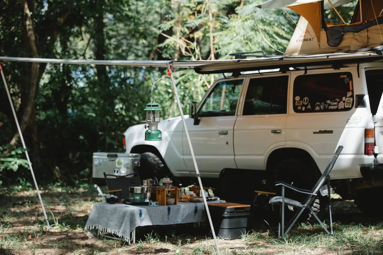 Overland SUV parked at a forest campsite with awning, lantern, and cooking setup