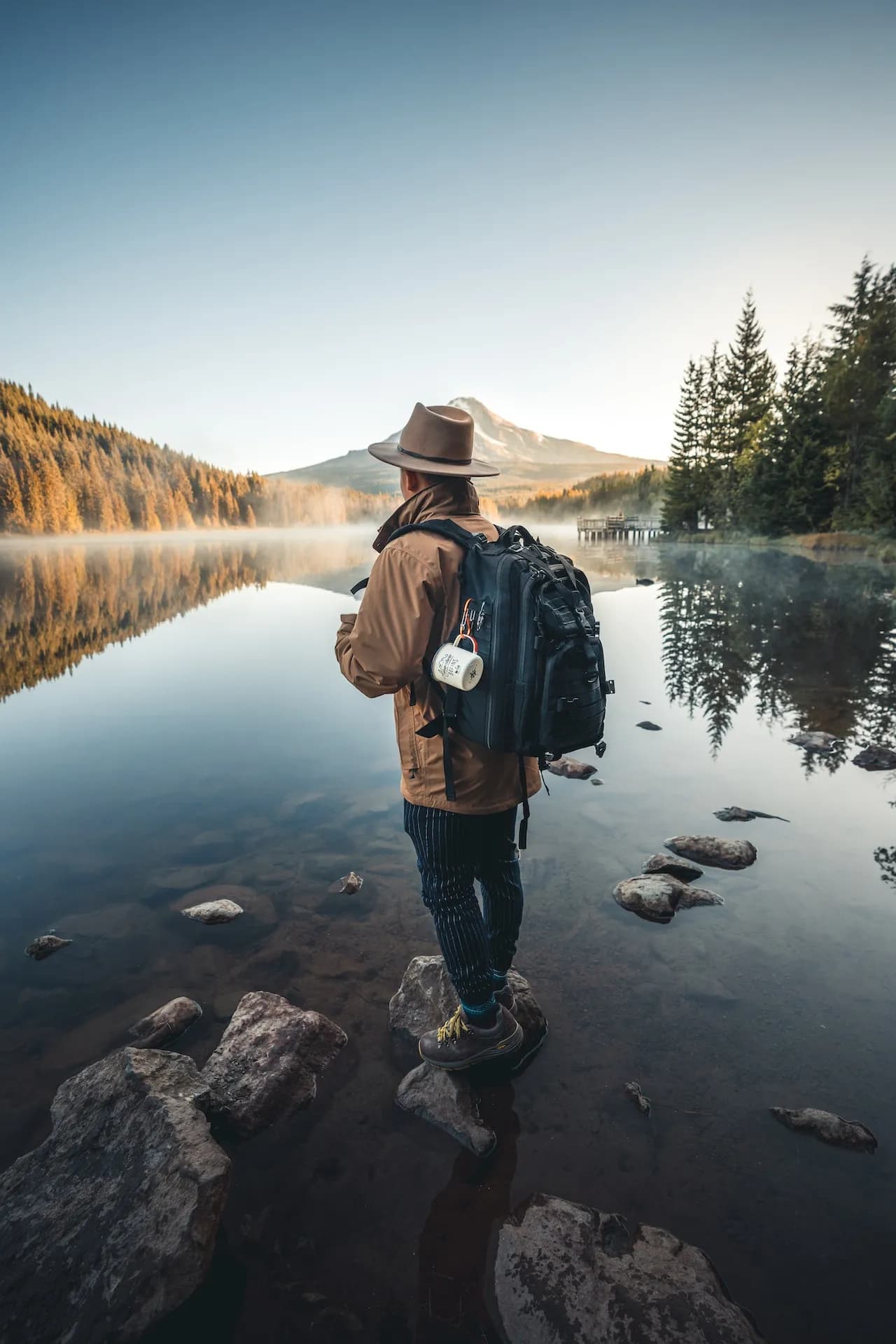 Guest writer with backpack looking out over a mountain lake at dawn